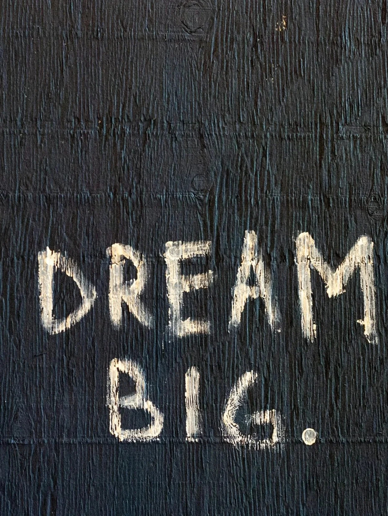 Black wooden surface with the words 'DREAM BIG.' written in white chalk.
