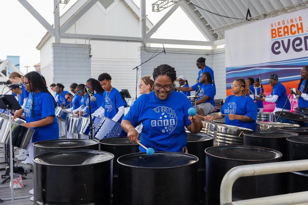 CAFE youth steel orchestra performs at Virginia Beach event, musicians in blue shirts playing steel pan drums on outdoor stage