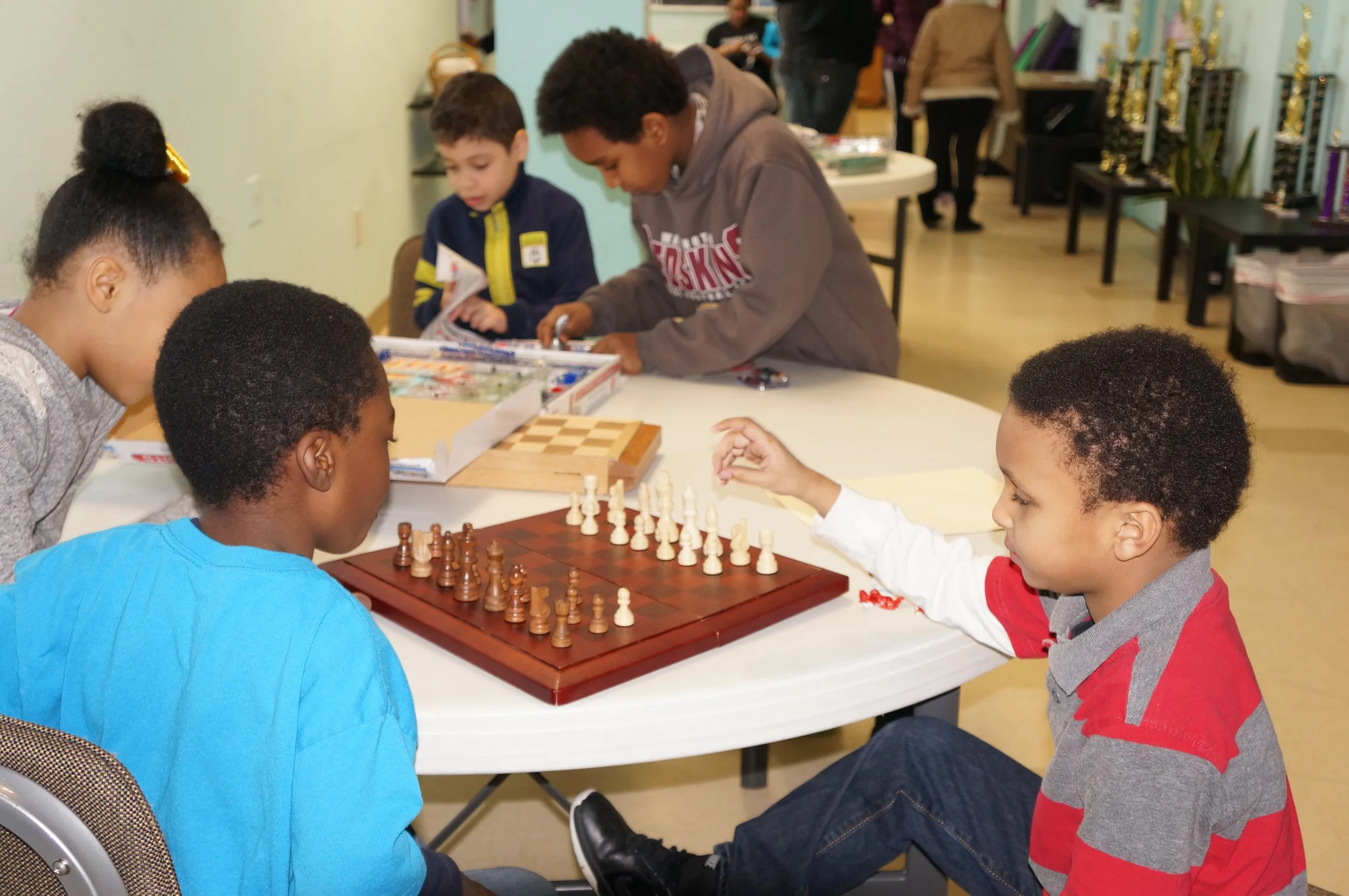 Children playing chess at a table in a classroom or a community center.
