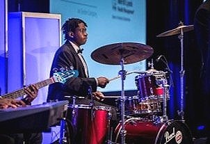 A young man playing a drum set during a live performance.