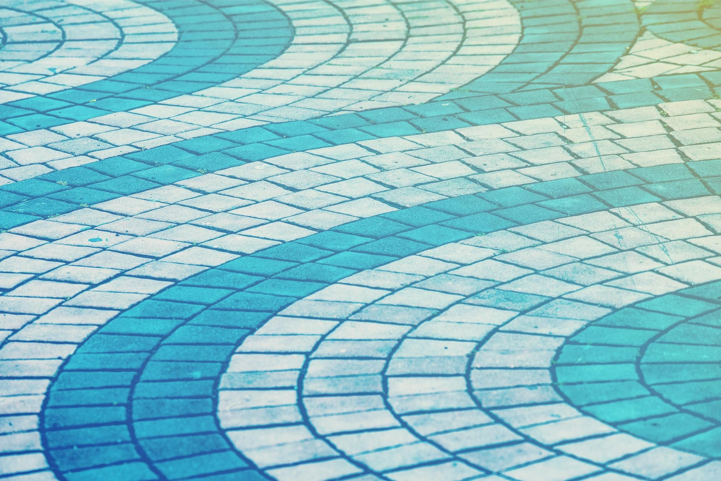 Close-up of a paved walkway with colorful, spiral and wave patterns formed by small bricks in shades of blue, white, and green.