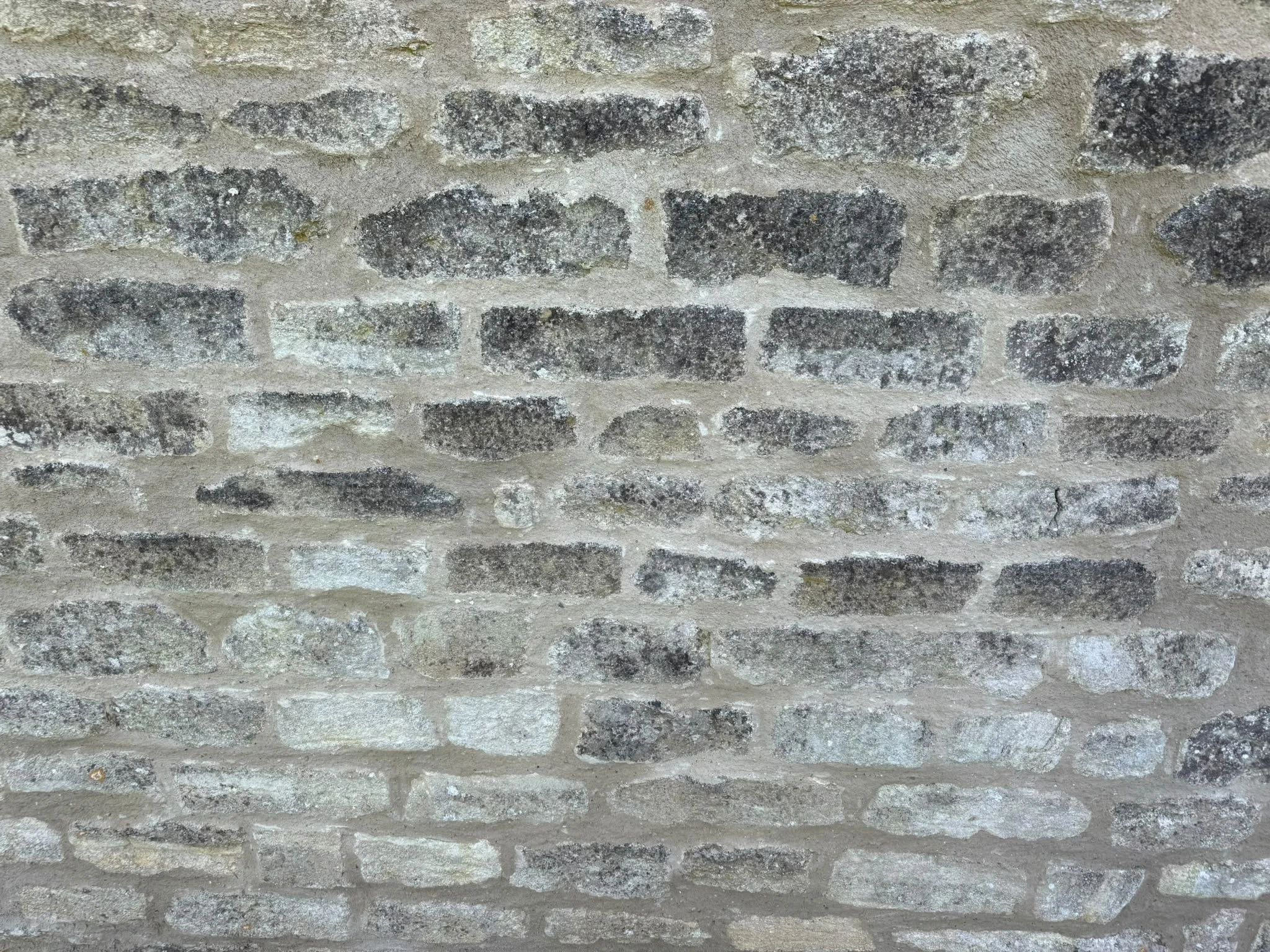 Close-up of a weathered brick wall with gray and black stones and light-colored mortar.
