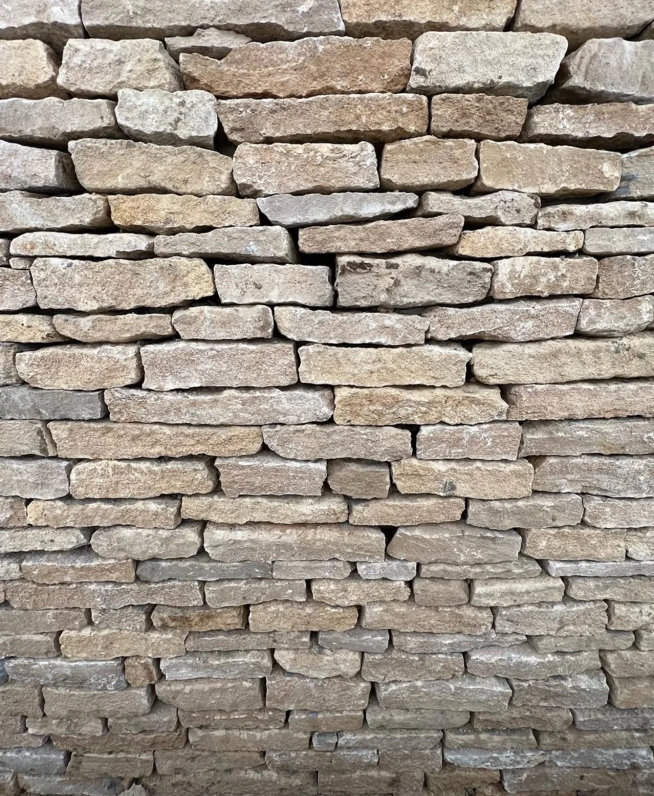 A close-up view of a stacked stone wall with rectangular and irregular stones in various shades of beige and light brown.