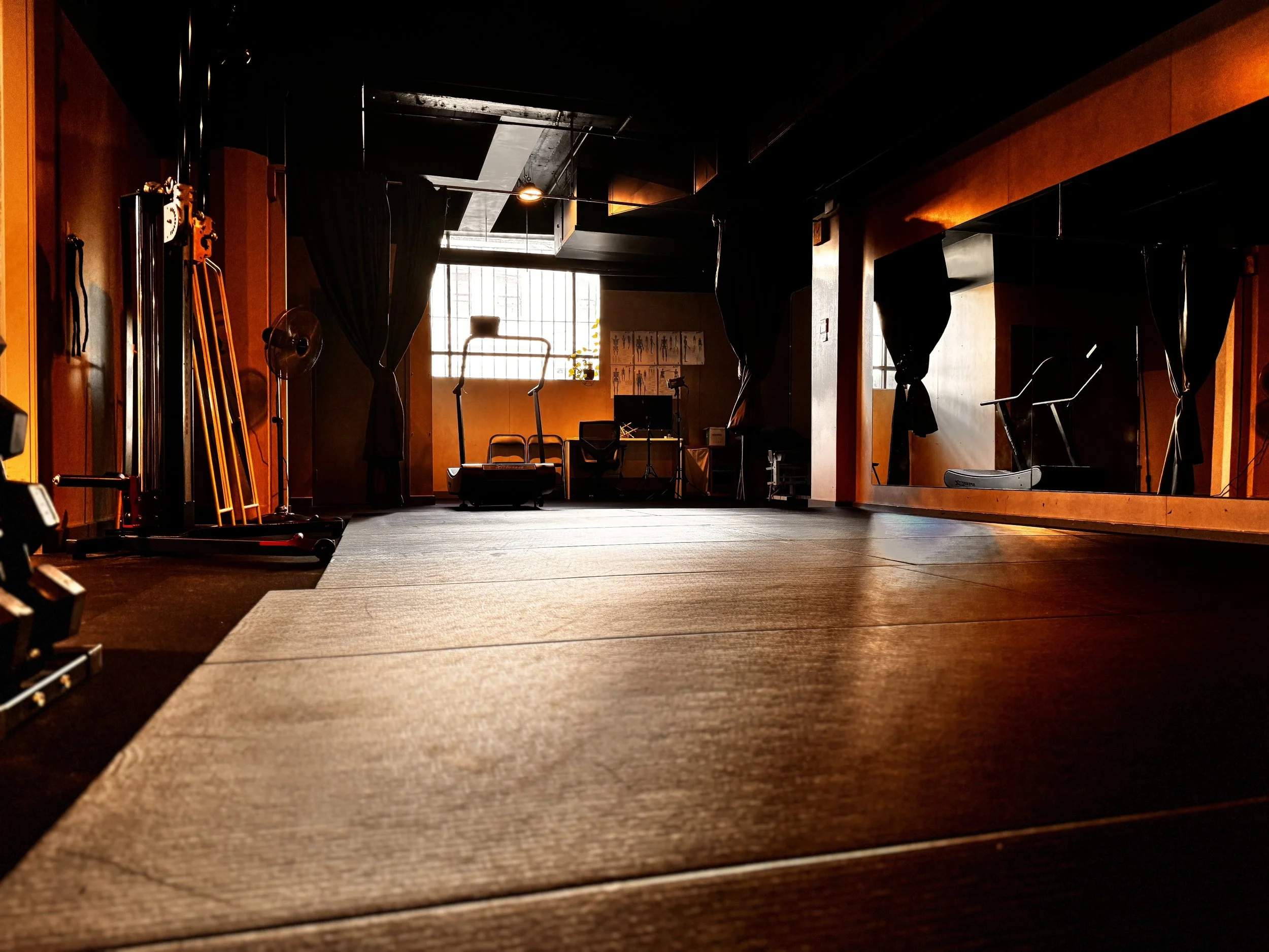 Empty gym or fitness studio with exercise equipment, mirrors, and sunlight coming through window, warm lighting.