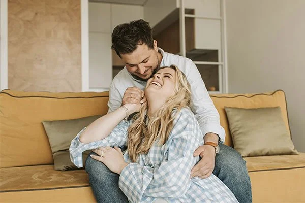 Couple on the couch laughing together, represents how you can regain your connection by working together with a couples therapy therapist in Los Angeles.