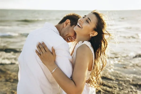 Couple hugging and smiling by the beach, represents how you can transform your dating life through guidance and coaching from a dating expert.