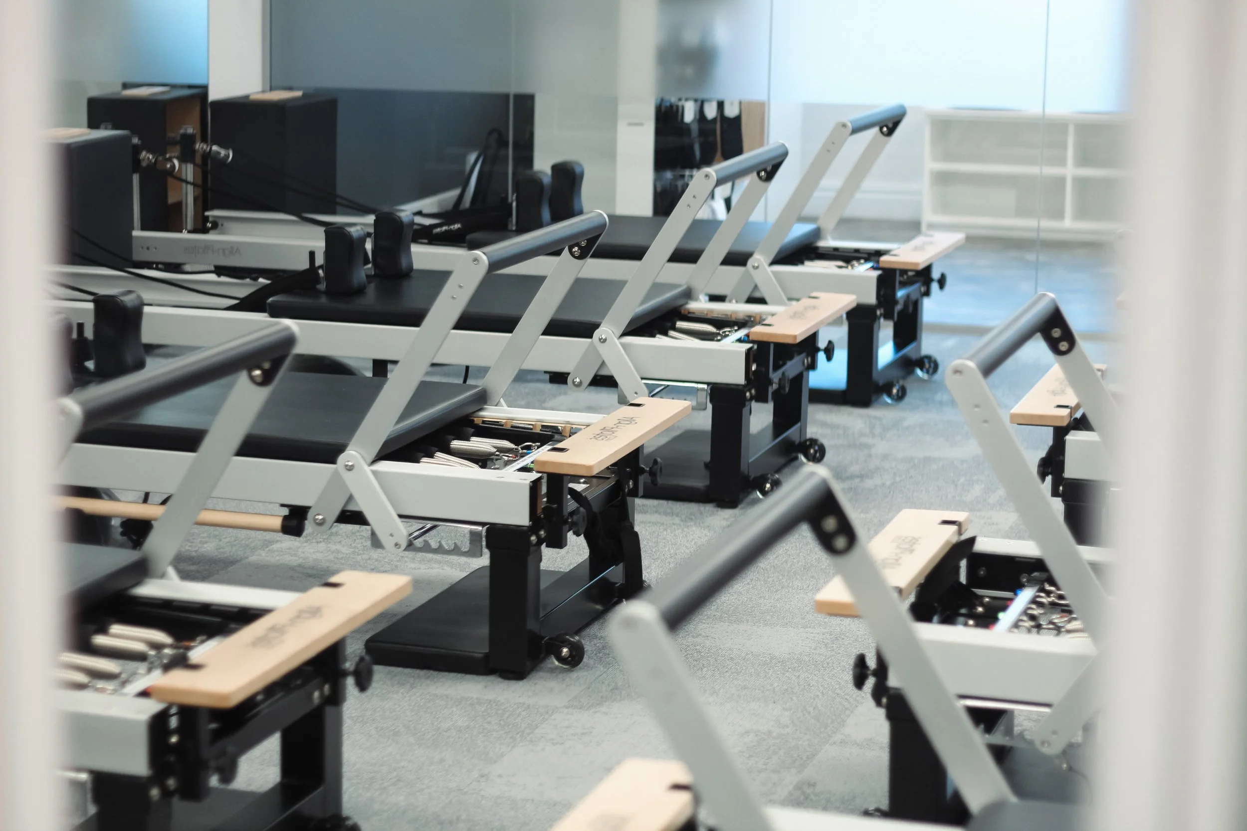 Rows of Pilates reformer machines with black padding and wooden platforms inside a modern fitness studio.