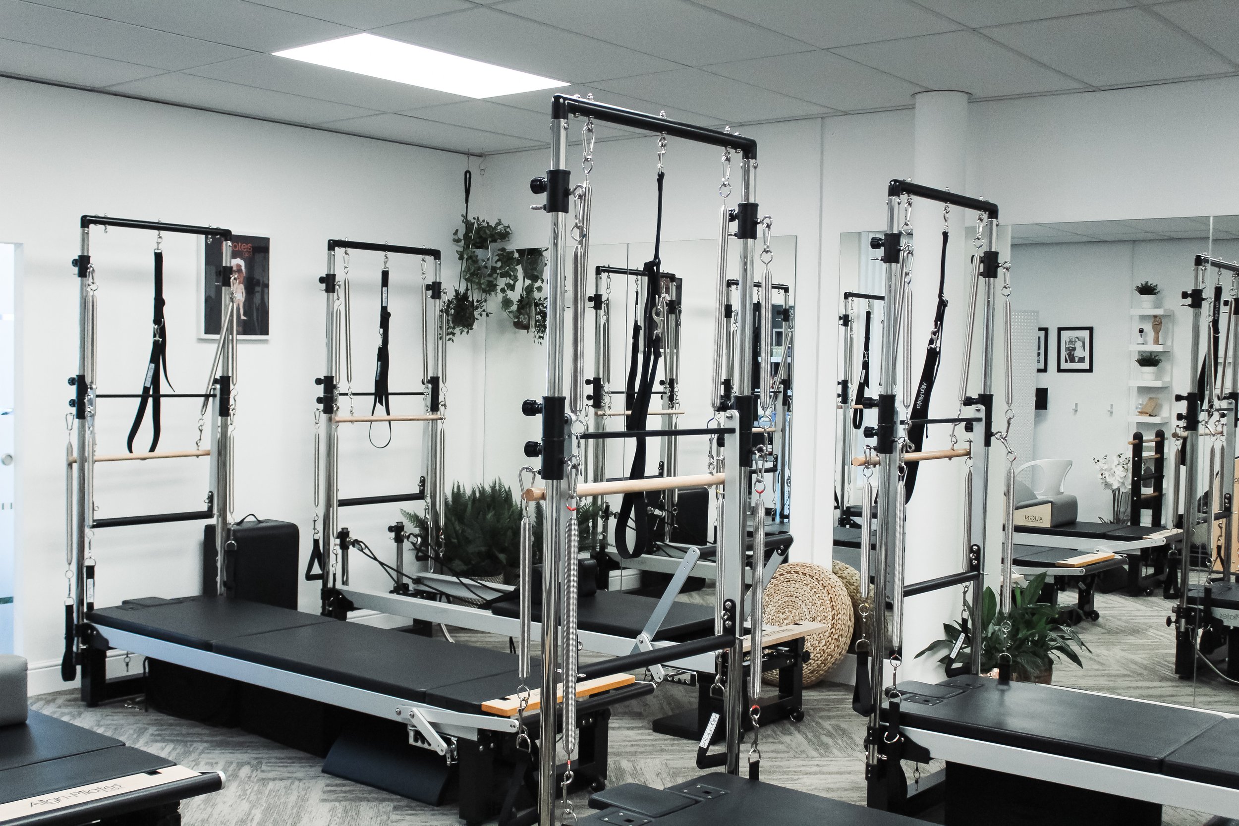 Fitness studio with pilates reformer machines and resistance equipment, neutral decor, framed photos, and plants.