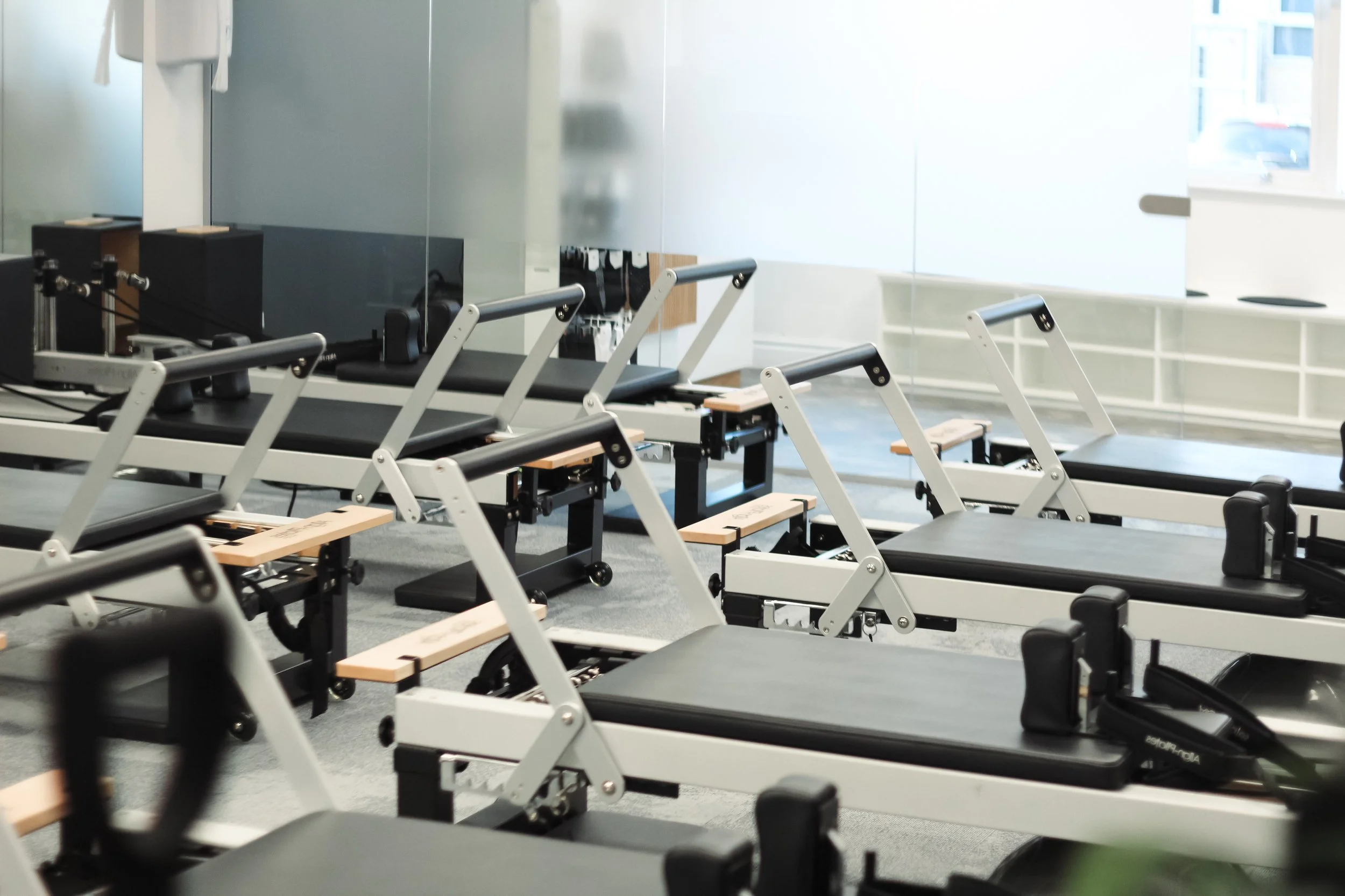 Empty Pilates reformer machines in a fitness studio with large windows.