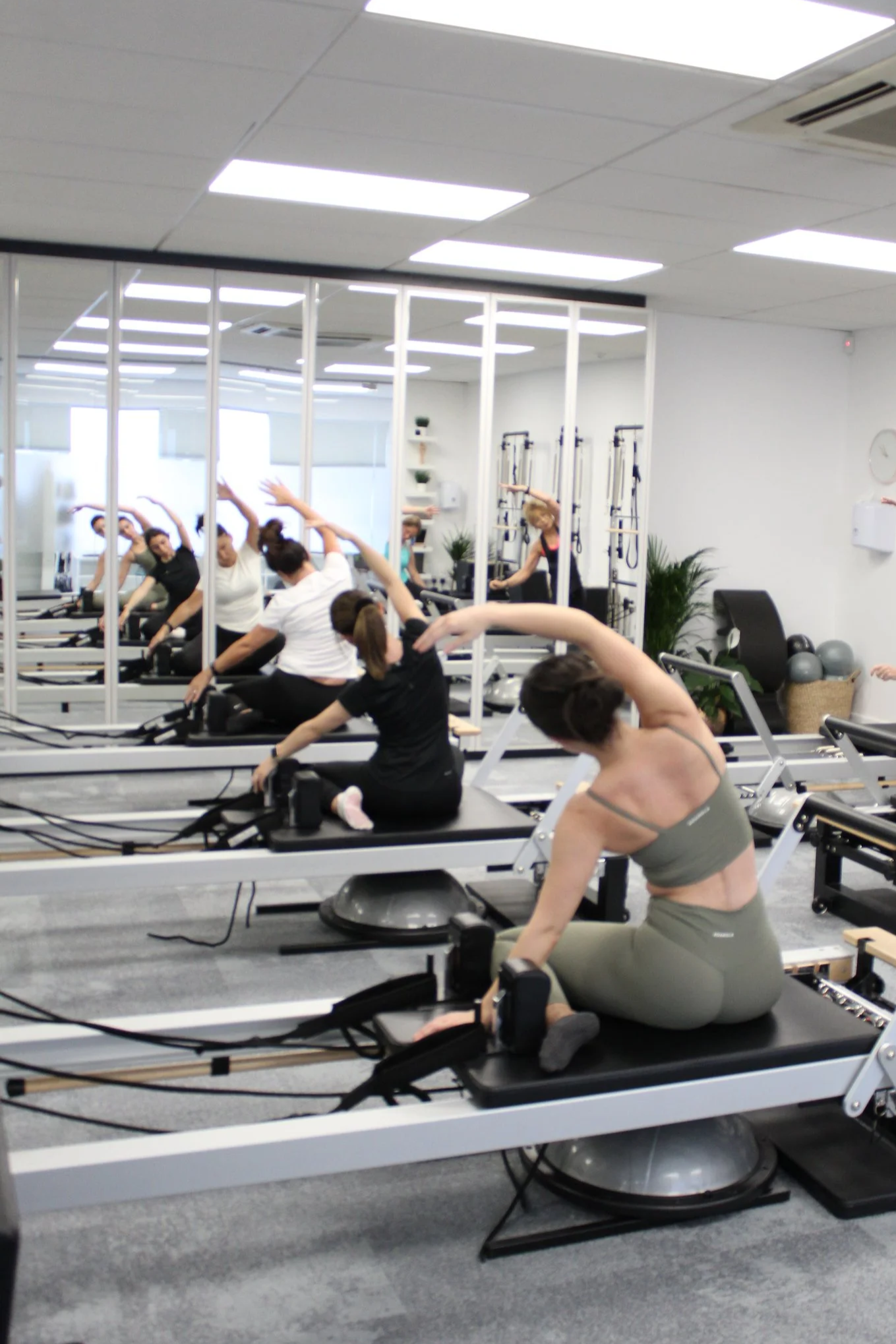 Women participating in a Pilates class using reformer exercise machines in a fitness studio with mirrors and workout equipment.