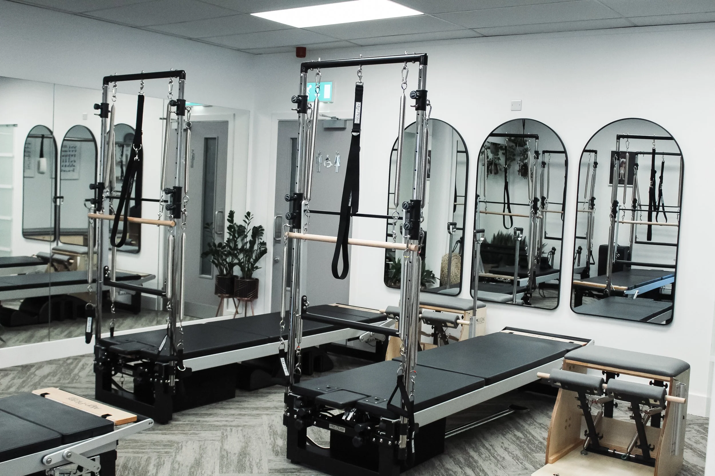 Pilates or fitness studio with reformer machines, mirrors on the wall, and a plant.