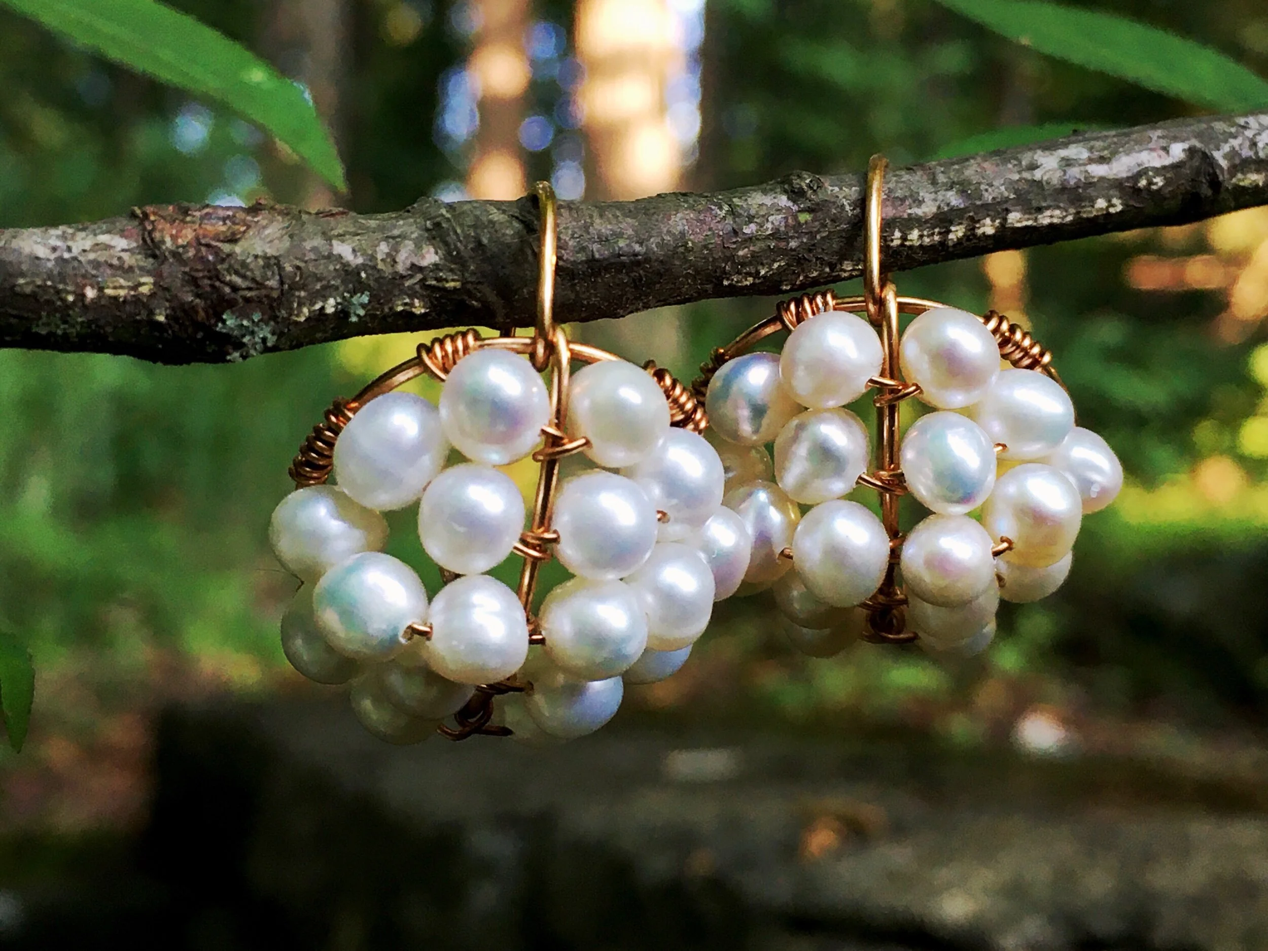 Pearl cluster earrings hanging from a branch in front of the woods