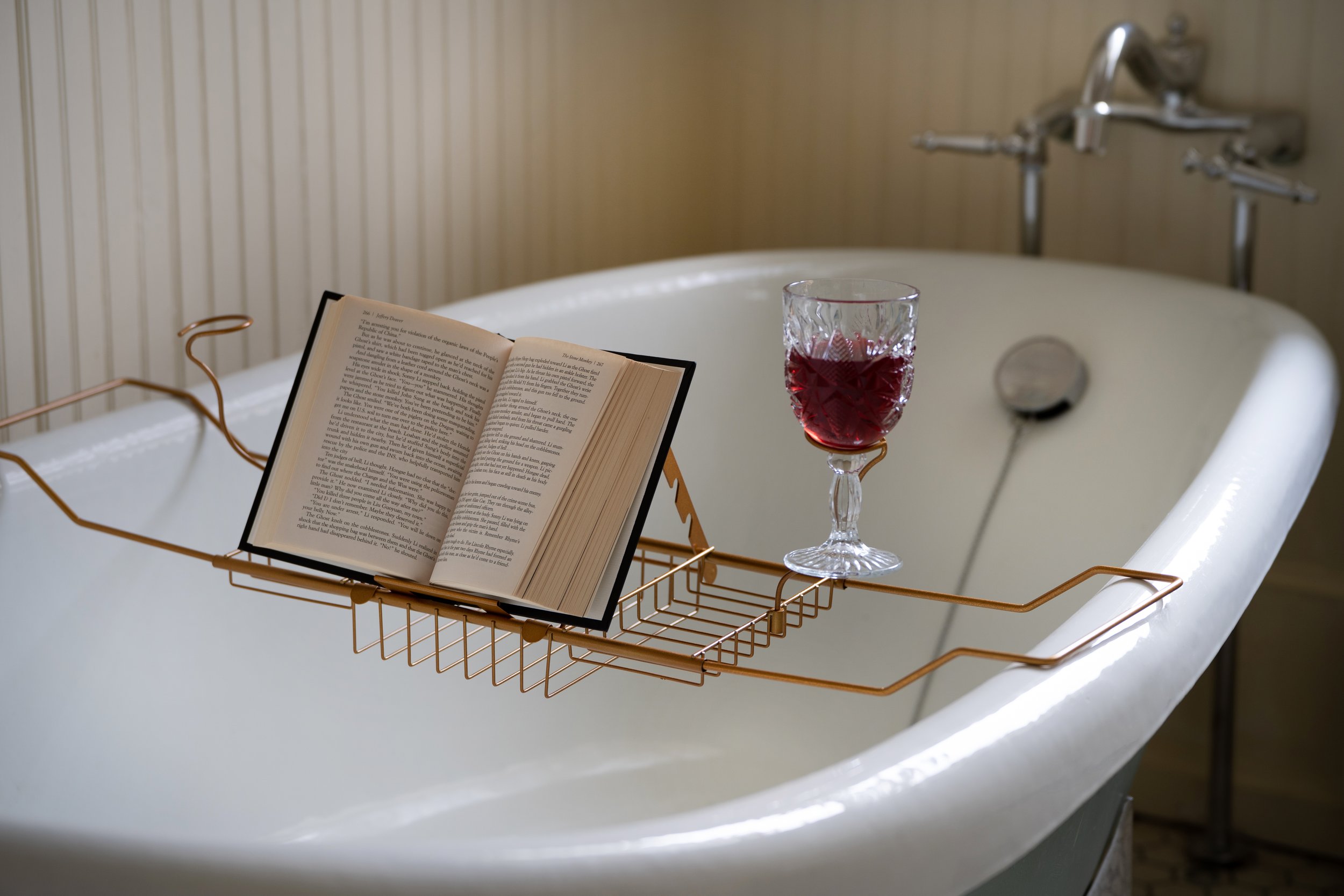 Bathtub with a book and a glass of red wine on a caddy