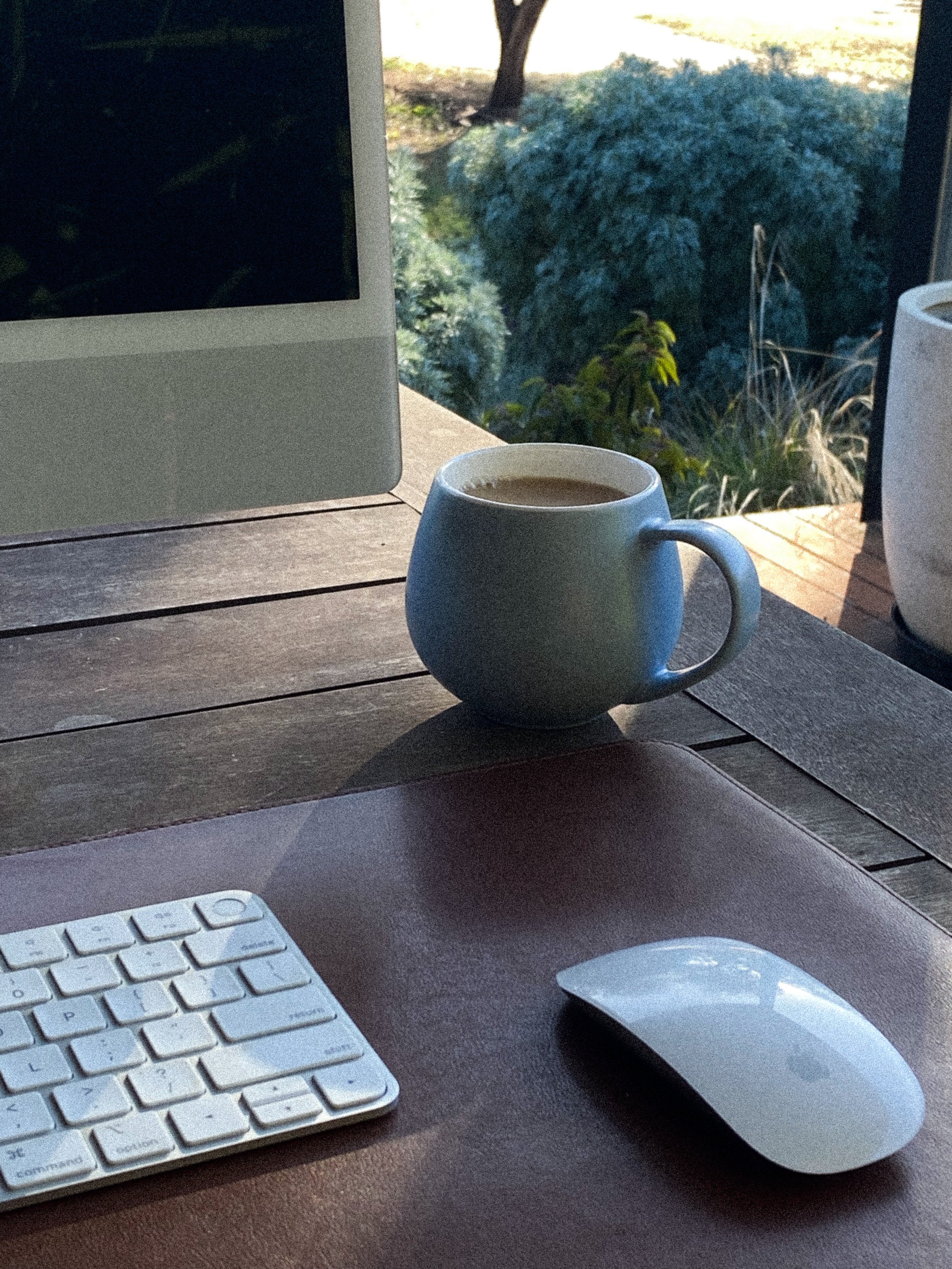 Abby Van Prooyen's work from home setup. Mac and keyboard with mouse on a wooden table outside.