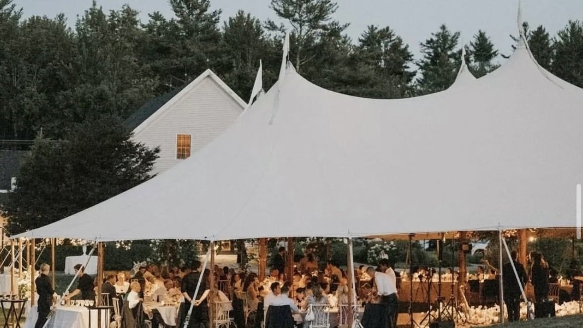 Outdoor event under a large white tent with guests seated at tables during evening.