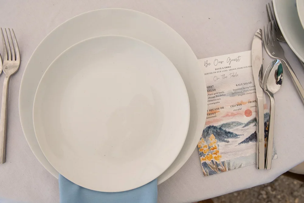 Empty white plates, fork, knife, and spoon on a table with a menu and a napkin.