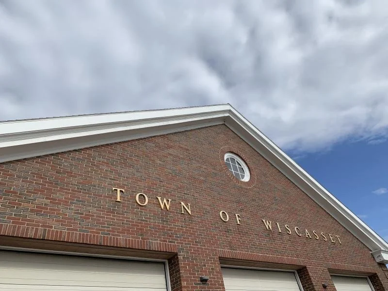Brick building with white trim and an arched window, with gold letters reading 'Town of Wiscasset' on the front.