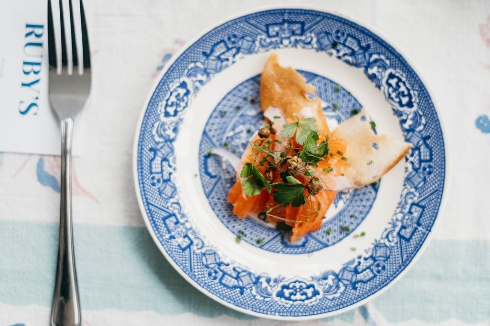 A plate with smoked salmon, garnished with herbs and onion, on a blue and white patterned plate.