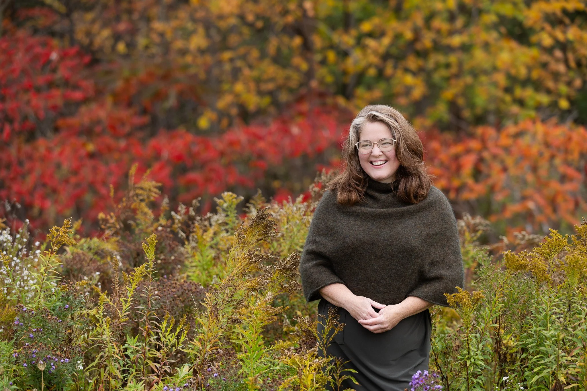 Woman standing in a field of wildflowers with autumn forest in the background.