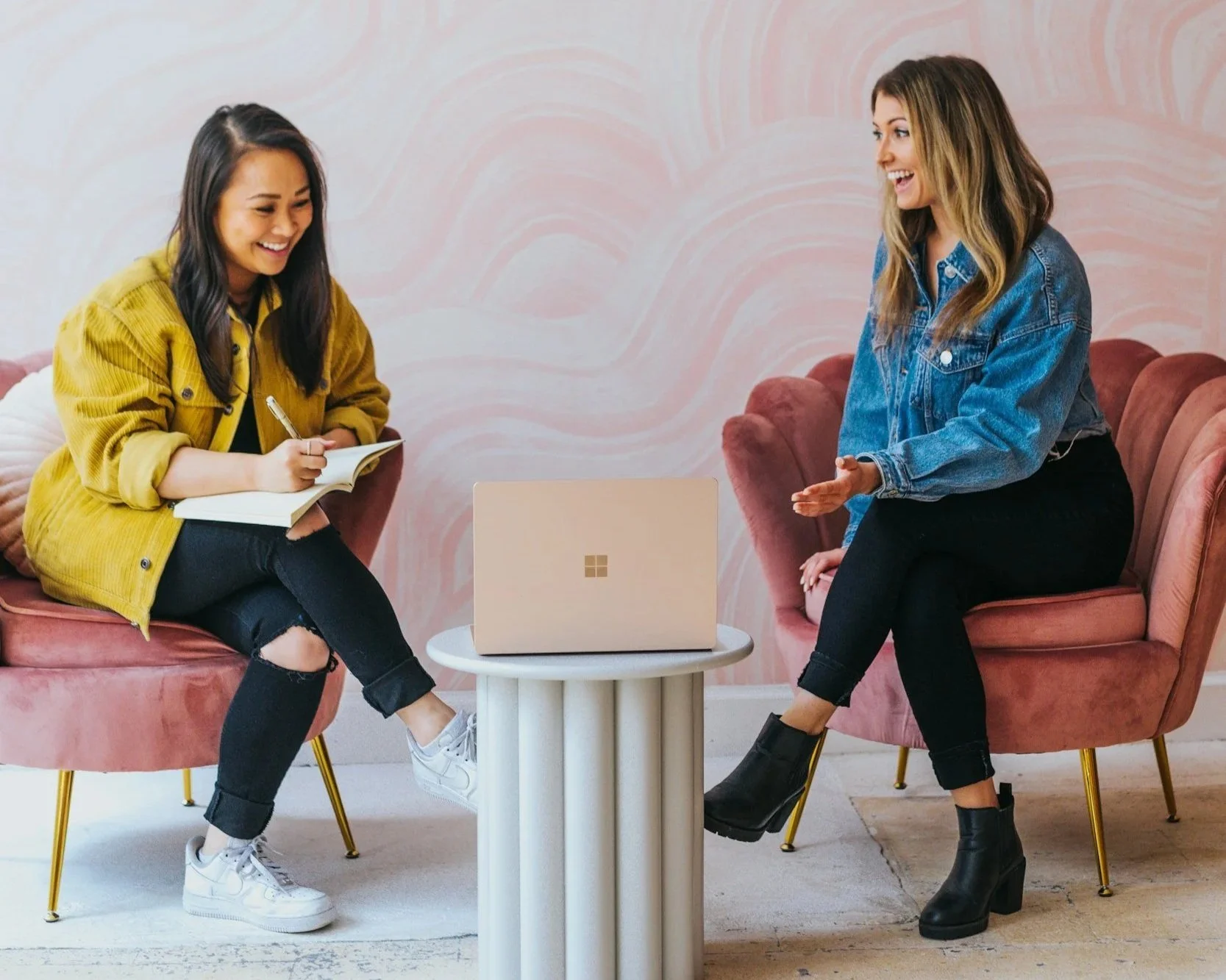 Two smiling women sitting in pink chairs talking and looking at a laptop. With the support of a trauma therapist in Sugar Land, TX you can incorporate the window of tolerance into your trauma and begin healing.