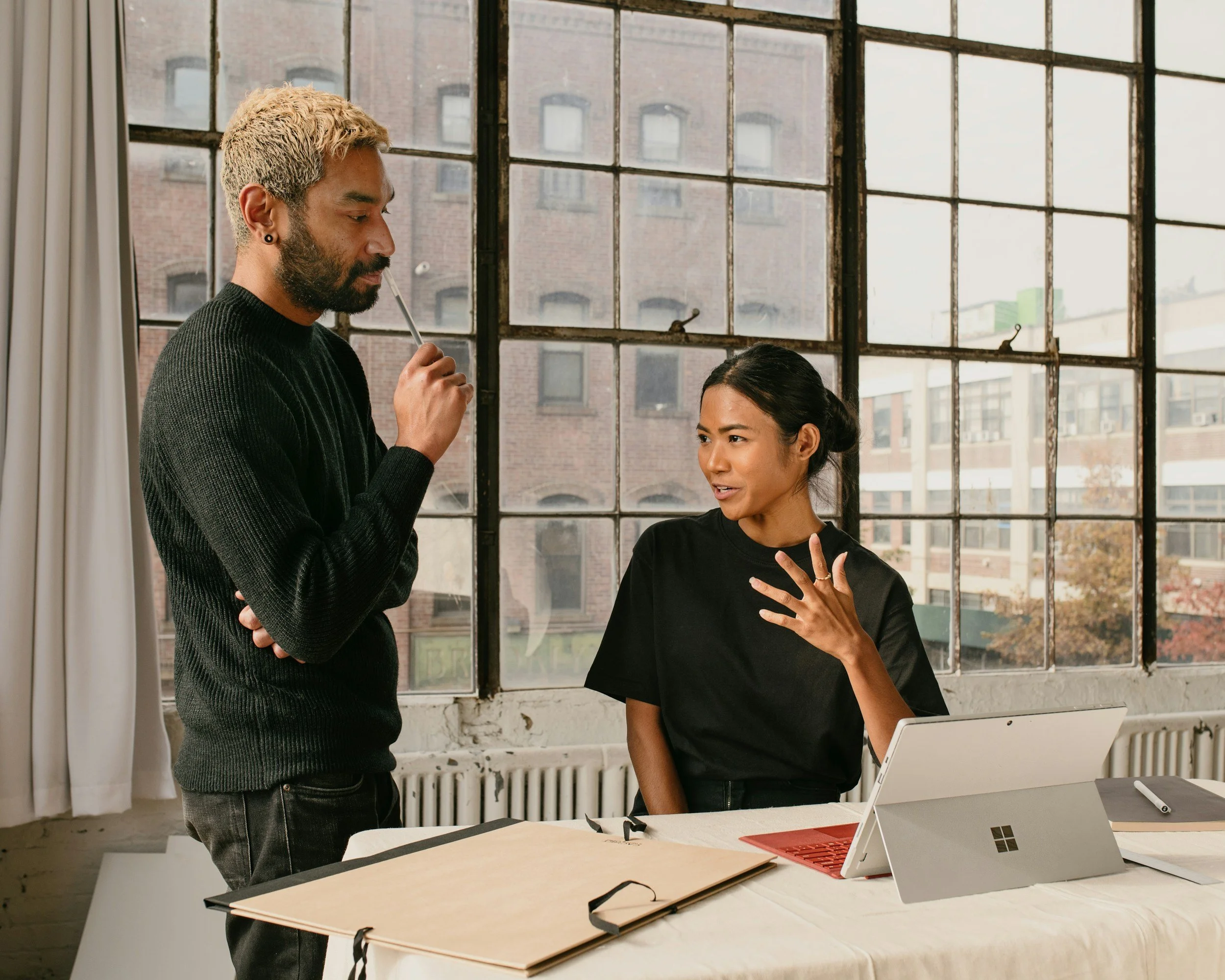 Man standing beside a woman sitting at a desk having a serious conversation. Learn to break the cycle of arguments with the support of a compassionate couples therapist in Sugar Land, TX.