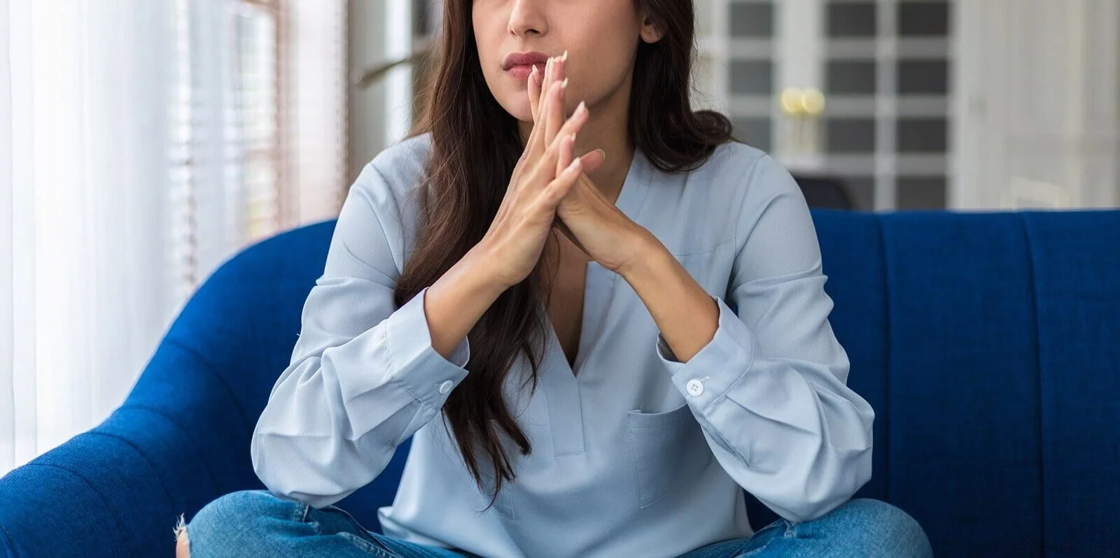 Image of a woman wearing blue clasping her hands together and thinking. Overcome your anxiety and burnout with the help of a skilled anxiety therapist in Sugar Land, TX.