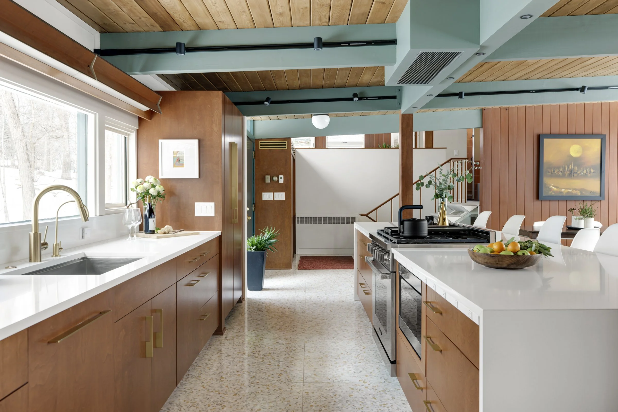 Modern kitchen with wood and pastel green accents, white countertops, stainless steel appliances, and a view of snow outside through a window.