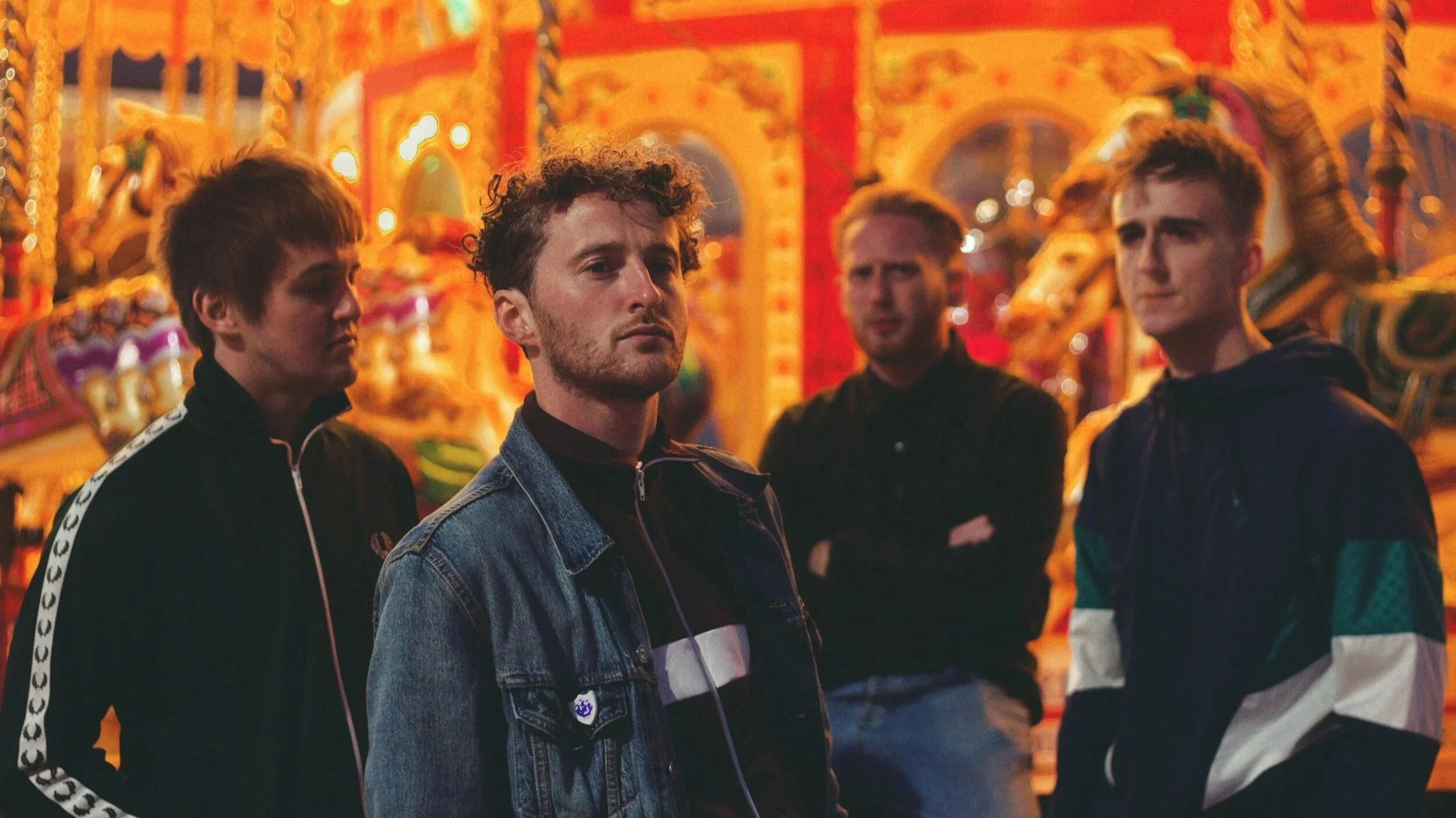The image features 4 men standing in front of a carousel at a fairground.