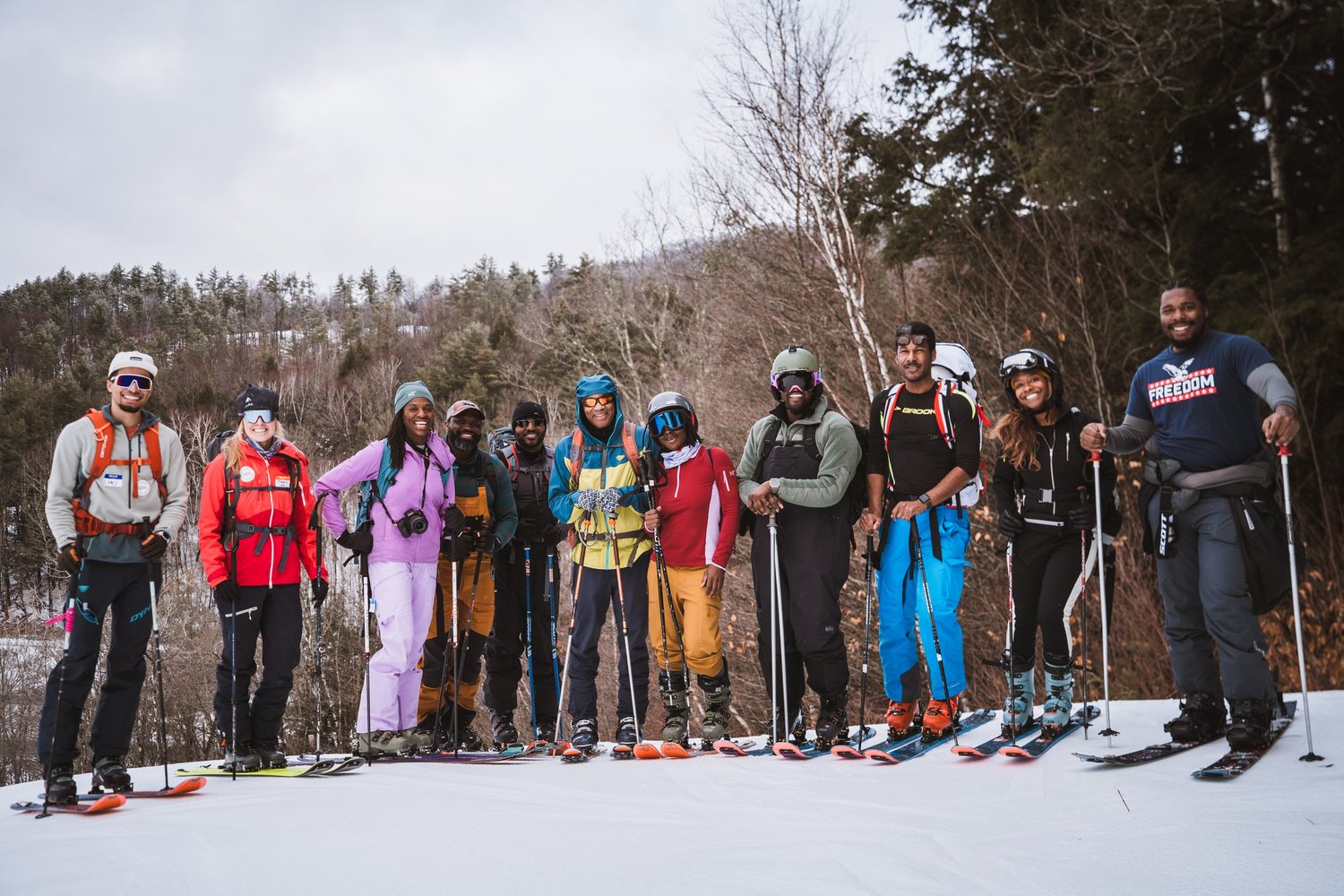 A large group of Inclusive Ski Touring participants at the summit on a bluebird day, skis and splitboards in the snow