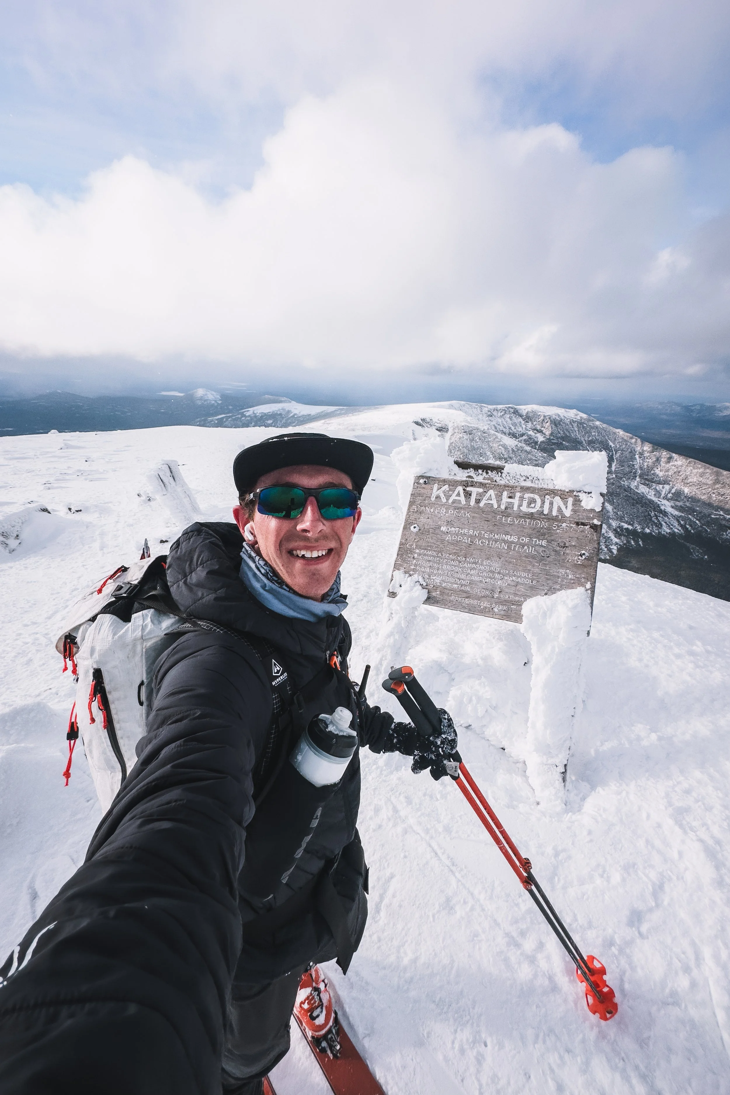Zach McCarthy at the Katahdin summit sign, skis on his pack