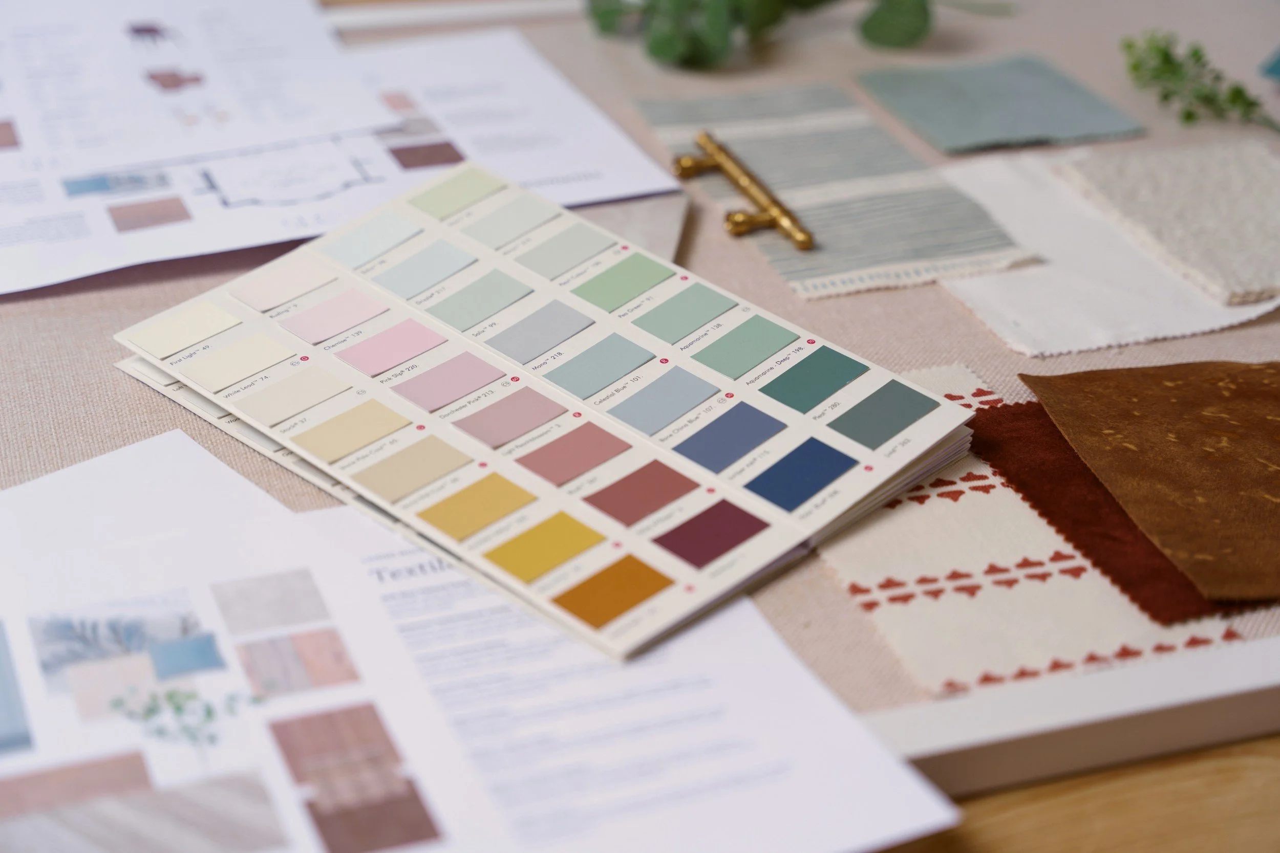 Color swatches and fabric samples arranged on a table, with design plans and a gold clip in the background.