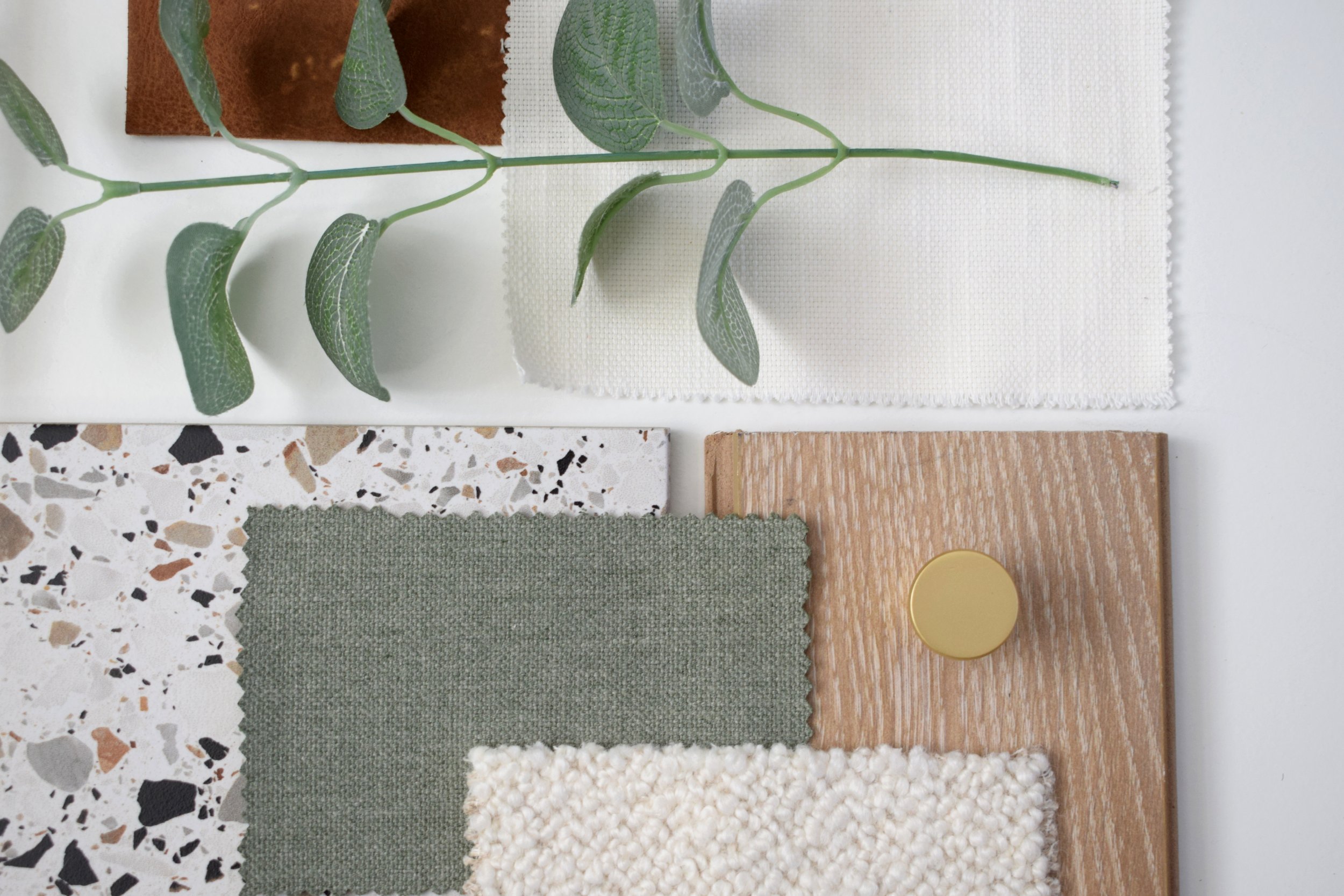 Sample display of various textile and material swatches, including terrazzo, woven fabrics, solid colors, wood, and a plant for interior design or material selection.