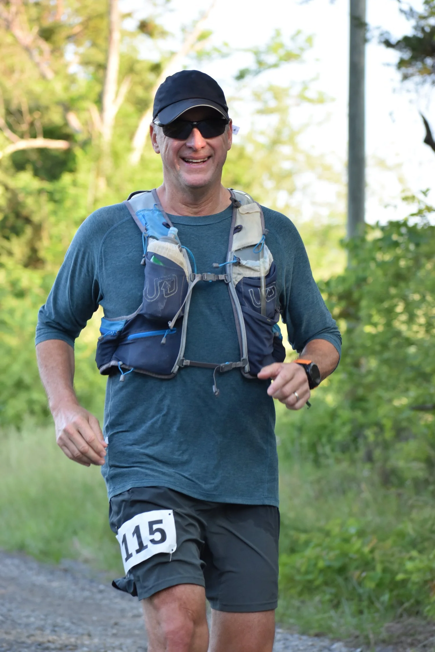 Ultrarunner John Mathis running a gravel trail in the Massanutten Mountains during the Old Dominion 100 in Virginia, wearing bib 115.