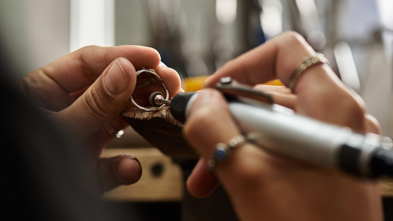 Close-up of a professional bench jeweler using a rotary polishing tool to finish a ring on a wooden bench pin.