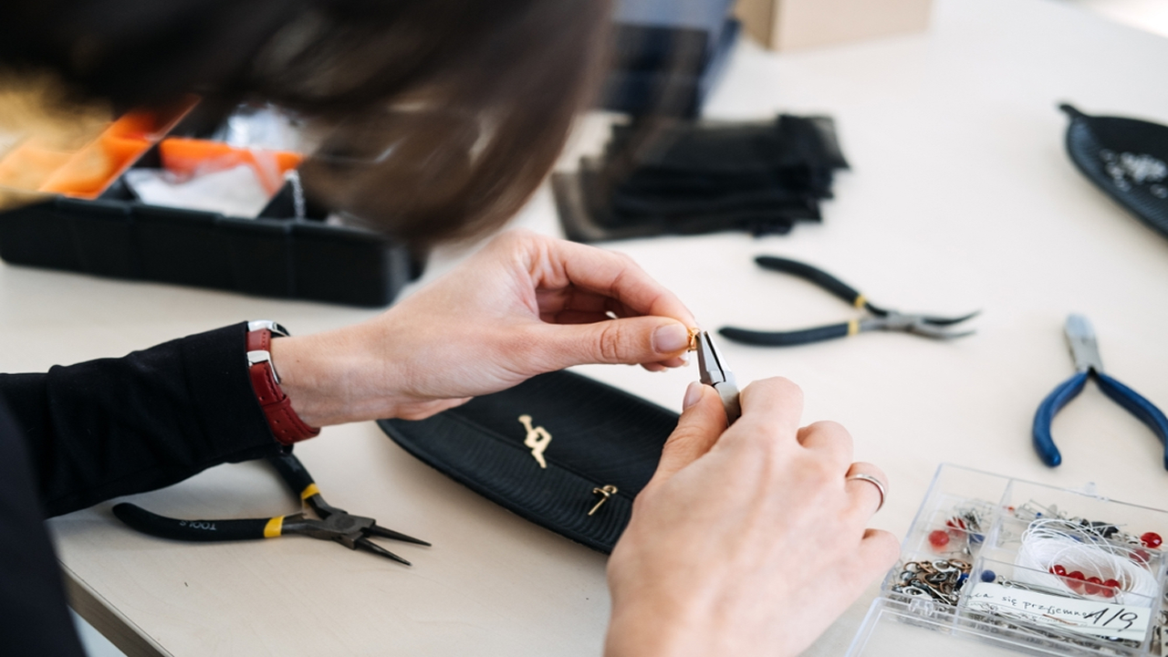 Close-up of a jewelry designer using hand pliers to craft a custom gold jewelry piece at a workbench.