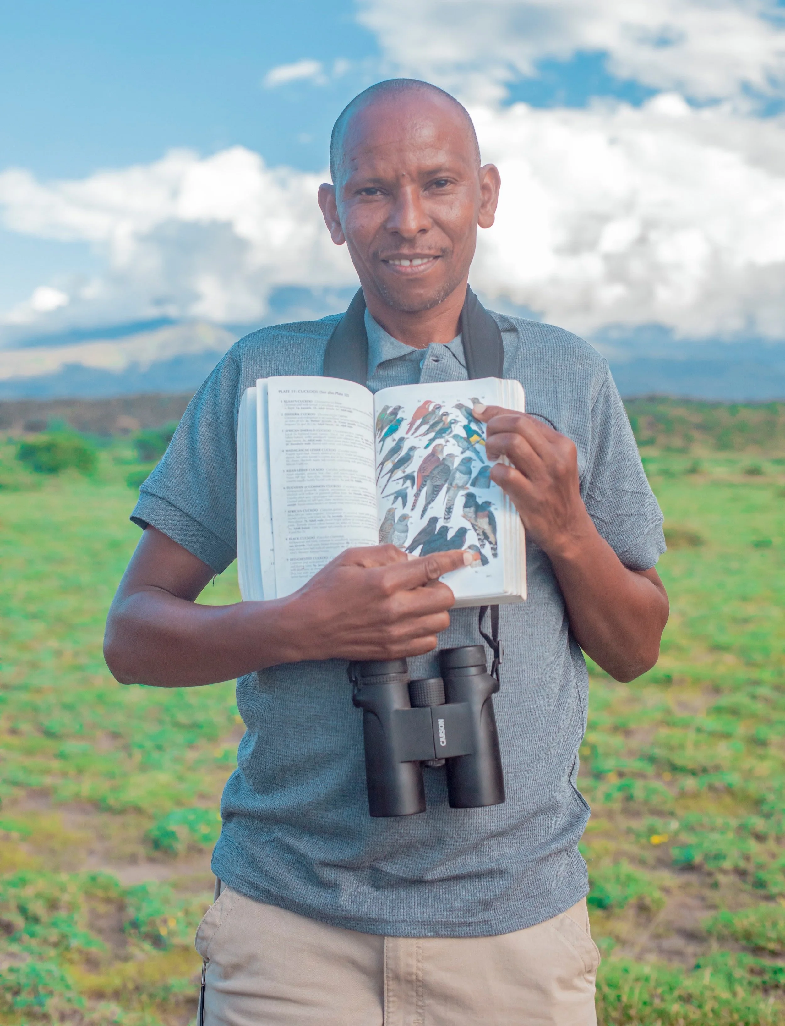 Person holding a bird field guide and binoculars outdoors