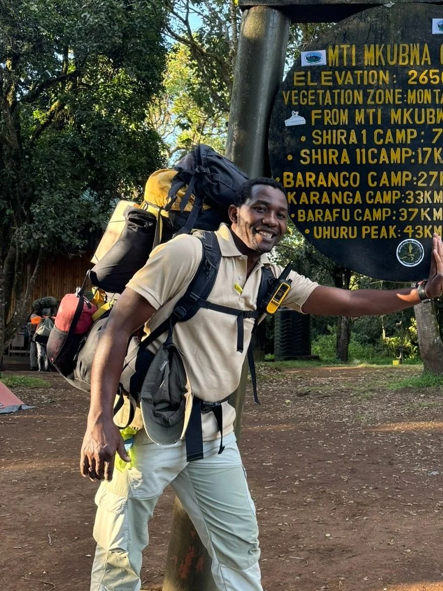 Man with backpack standing next to a signpost in a forested area.