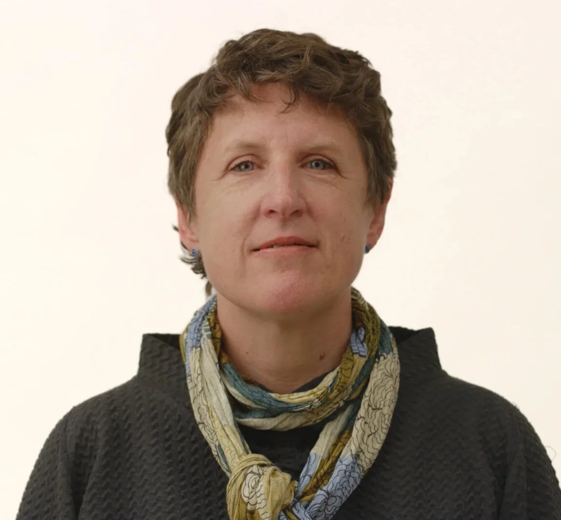 Susie wears a grey sweater and a colorful yellow and blue scarf