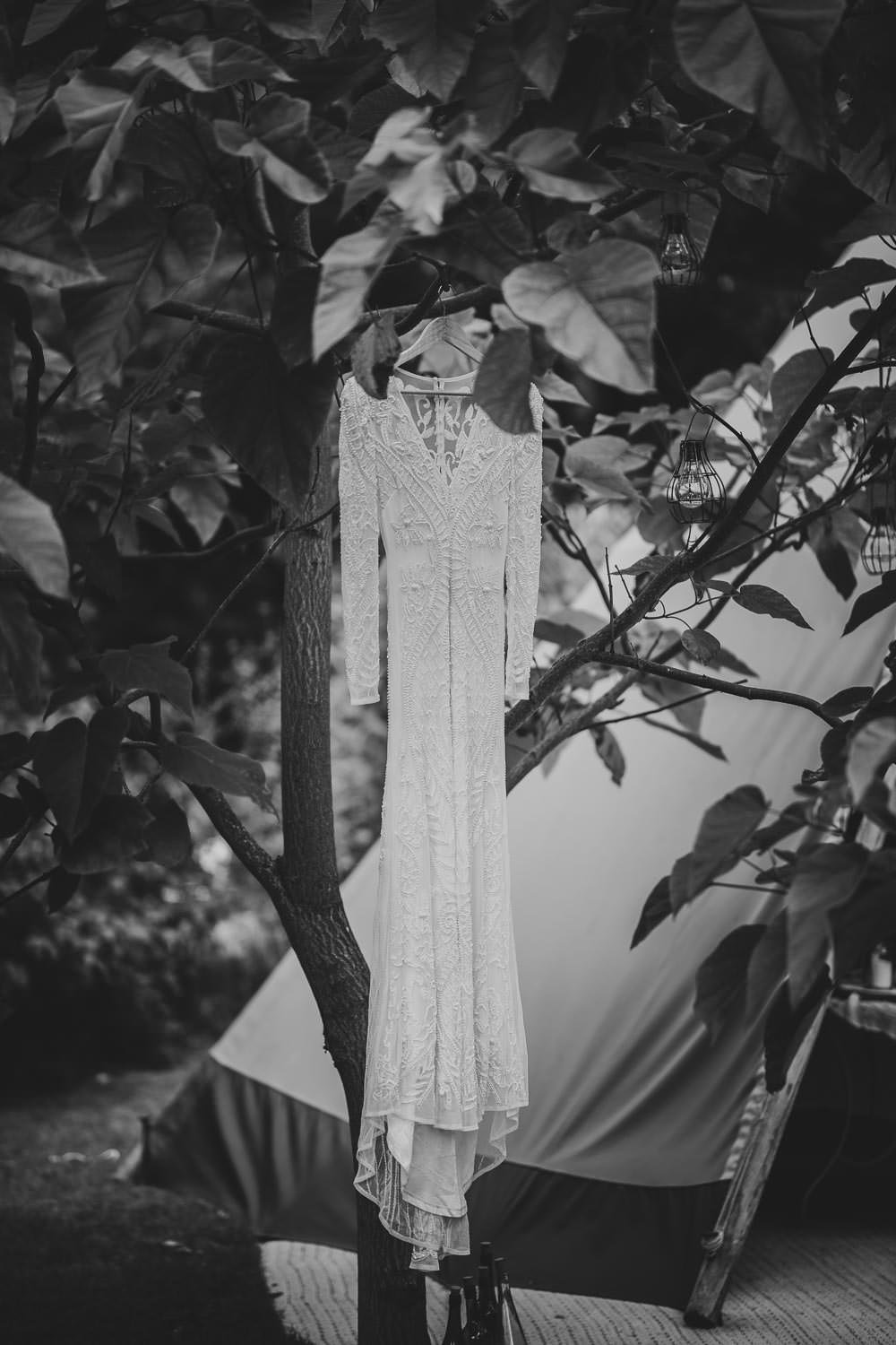 Lace wedding dress hanging on display amongst green foliage and trees