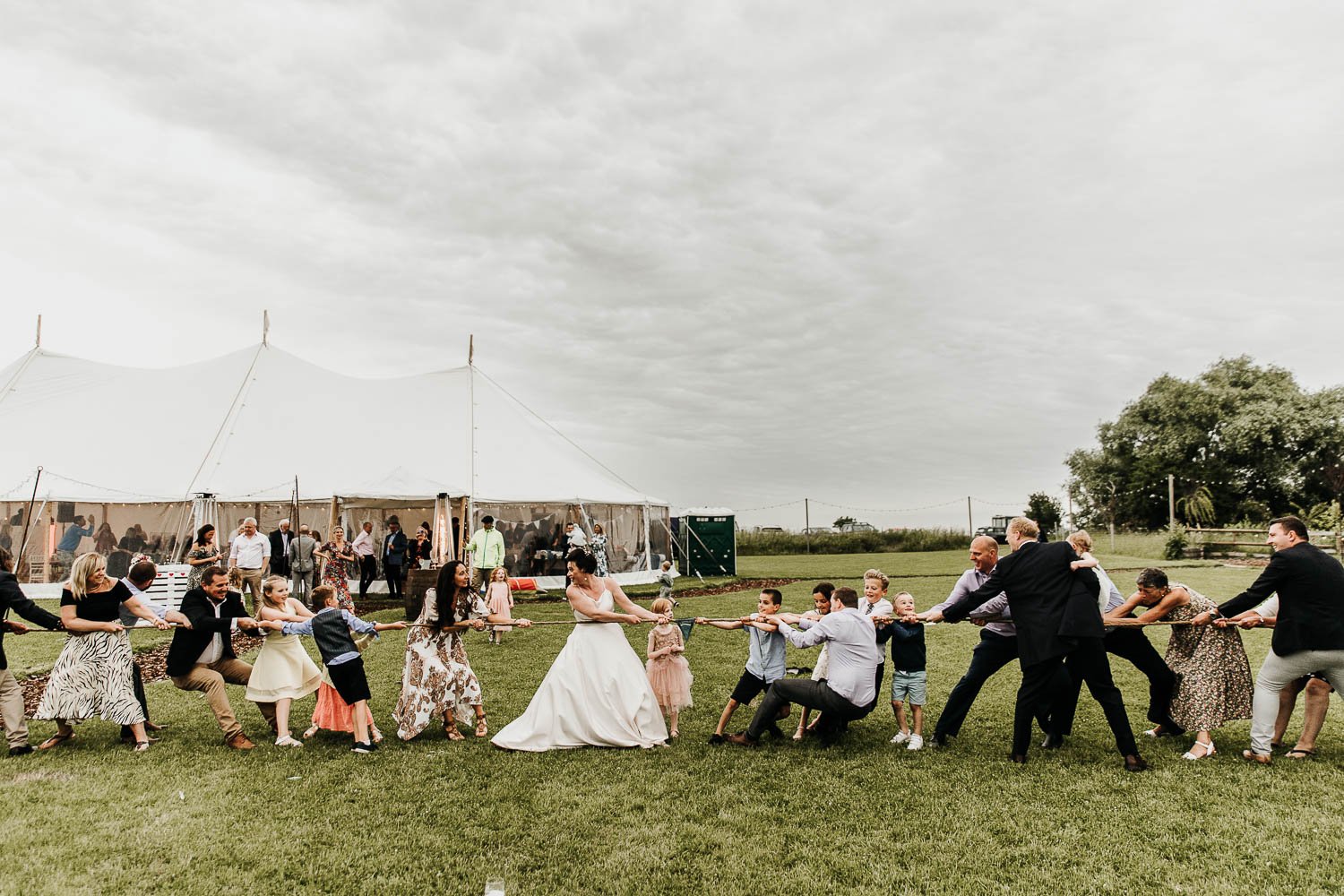 Guests battling it out in a game of tug of war at a rustic farm wedding venue
