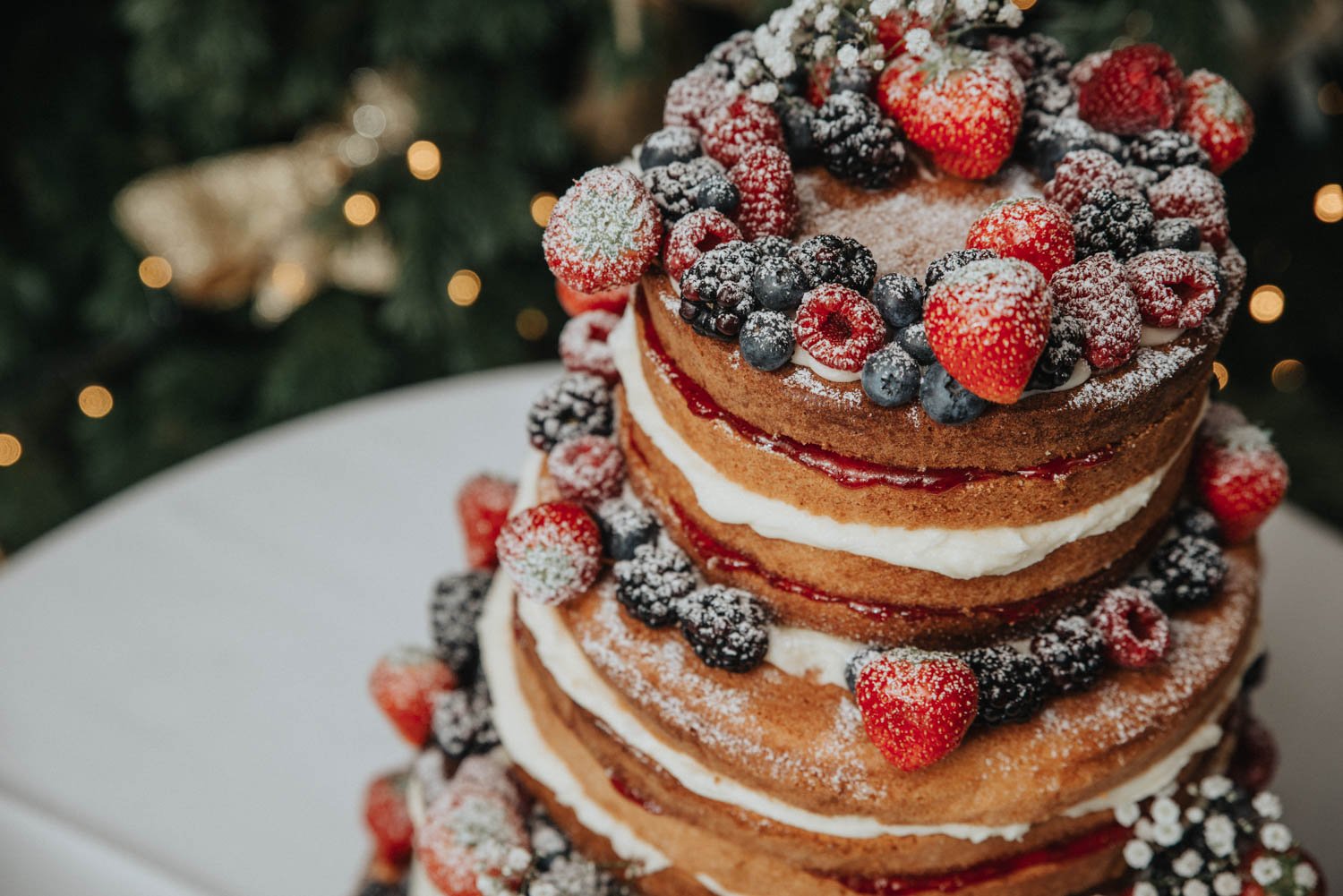 Winter fruit wedding cake with raw sponge, raspberries and blackberries with icing sugar dusting