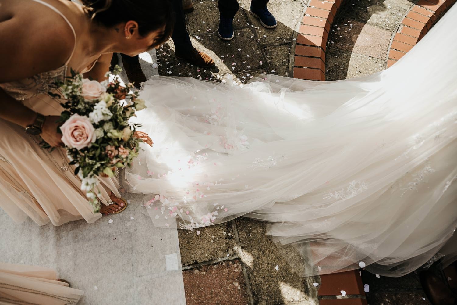 Confetti scattered across the train of brides wedding dress with bridesmaid helping to straighten train