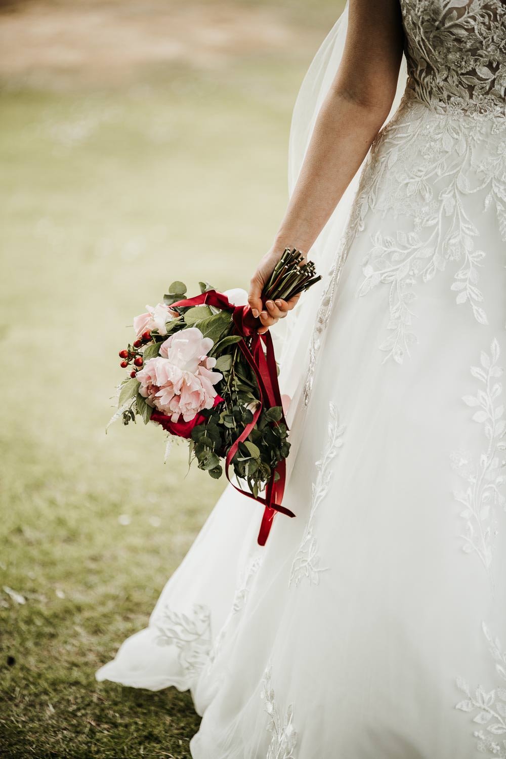 Rose bouquet held beside wedding dress skirt by bride