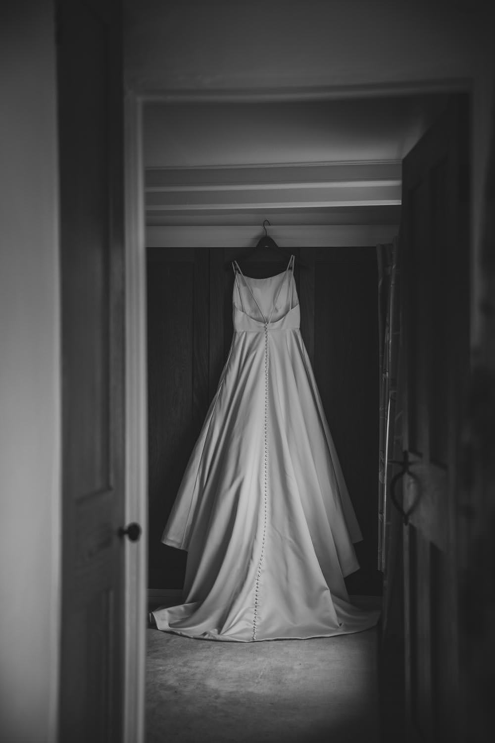 Button backed wedding dress hanging on wardrobe of brides home with window light