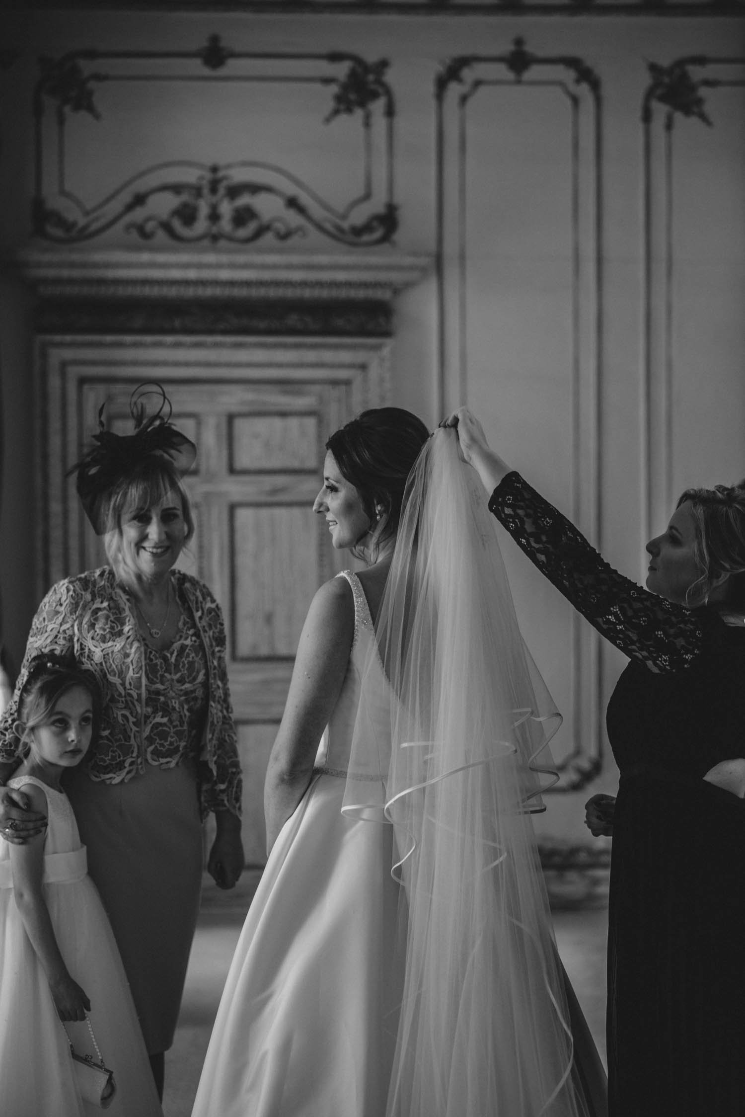 Bride putting veil on in bridal suite with help