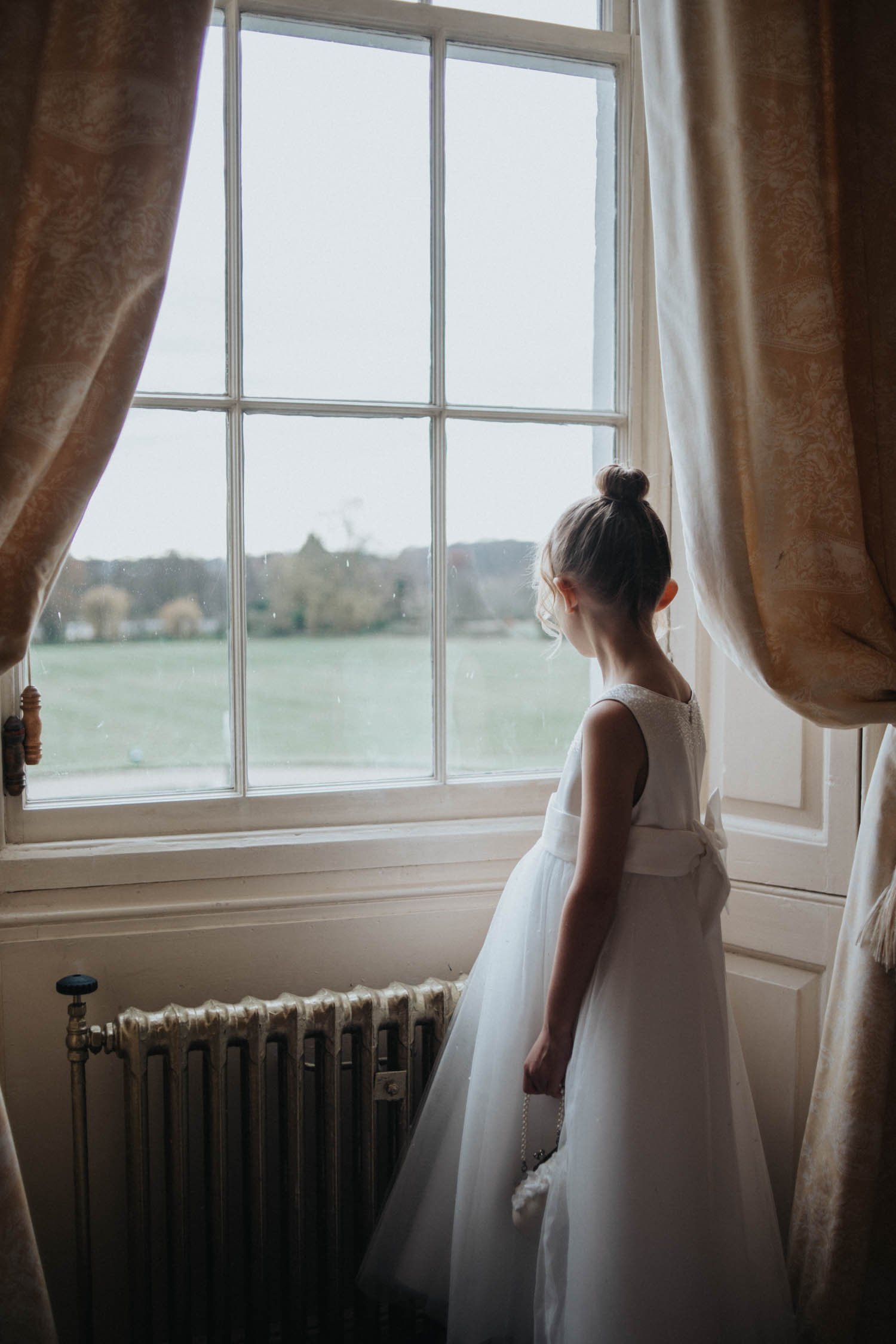 Flower girl looking out of window of bridal suite with soft dress