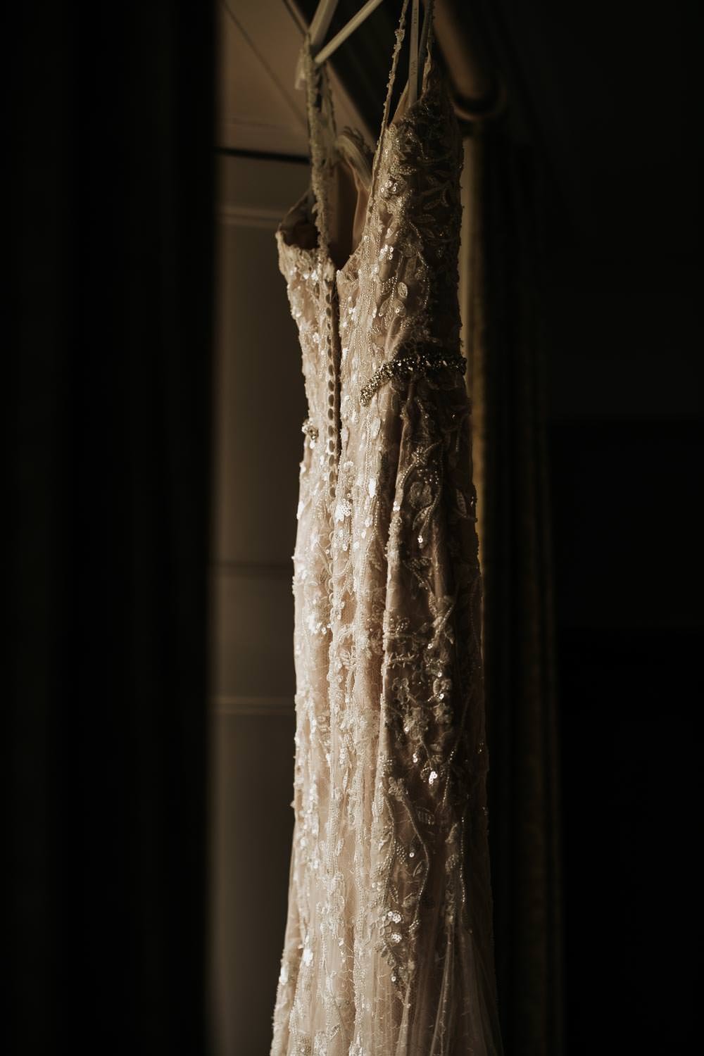 Lace wedding dress hanging in the window sunlight 