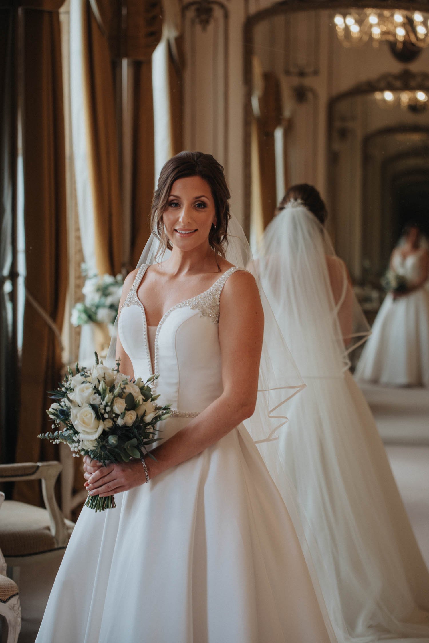 Bride with bouquet in bridal suite with large mirror in the background