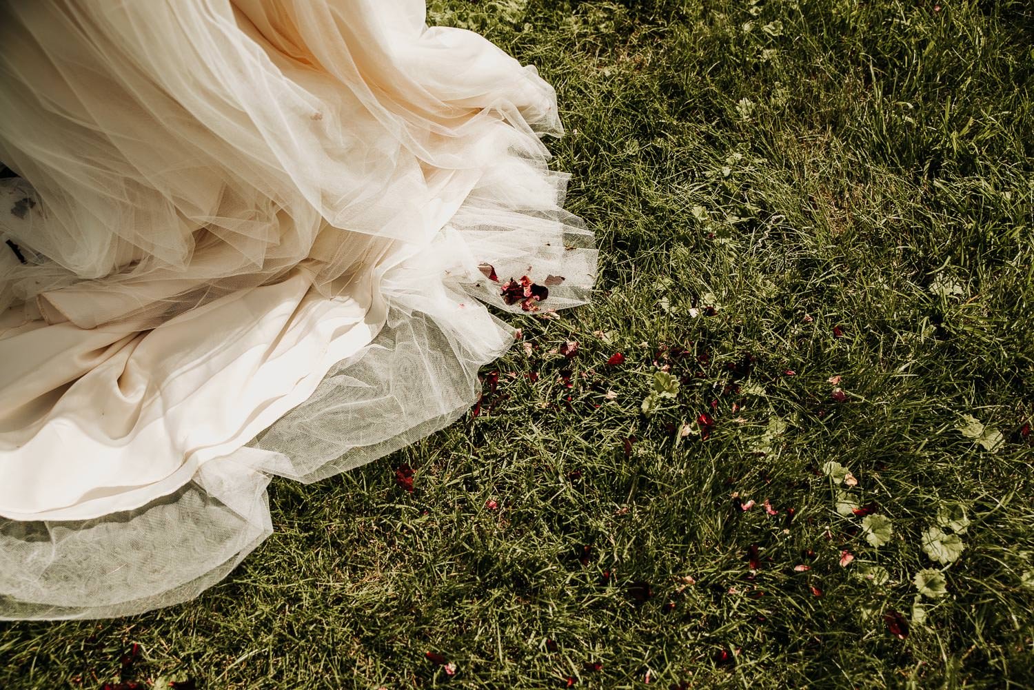 Wedding dress trailing on the grass with rose petal confetti at wedding party