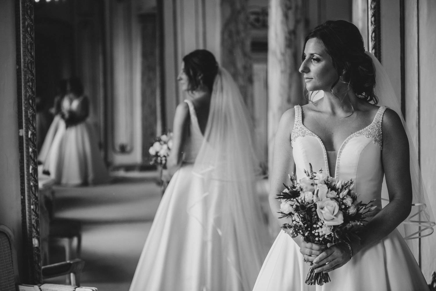 Bride stood in front of large mirror of bridal suite with reflections